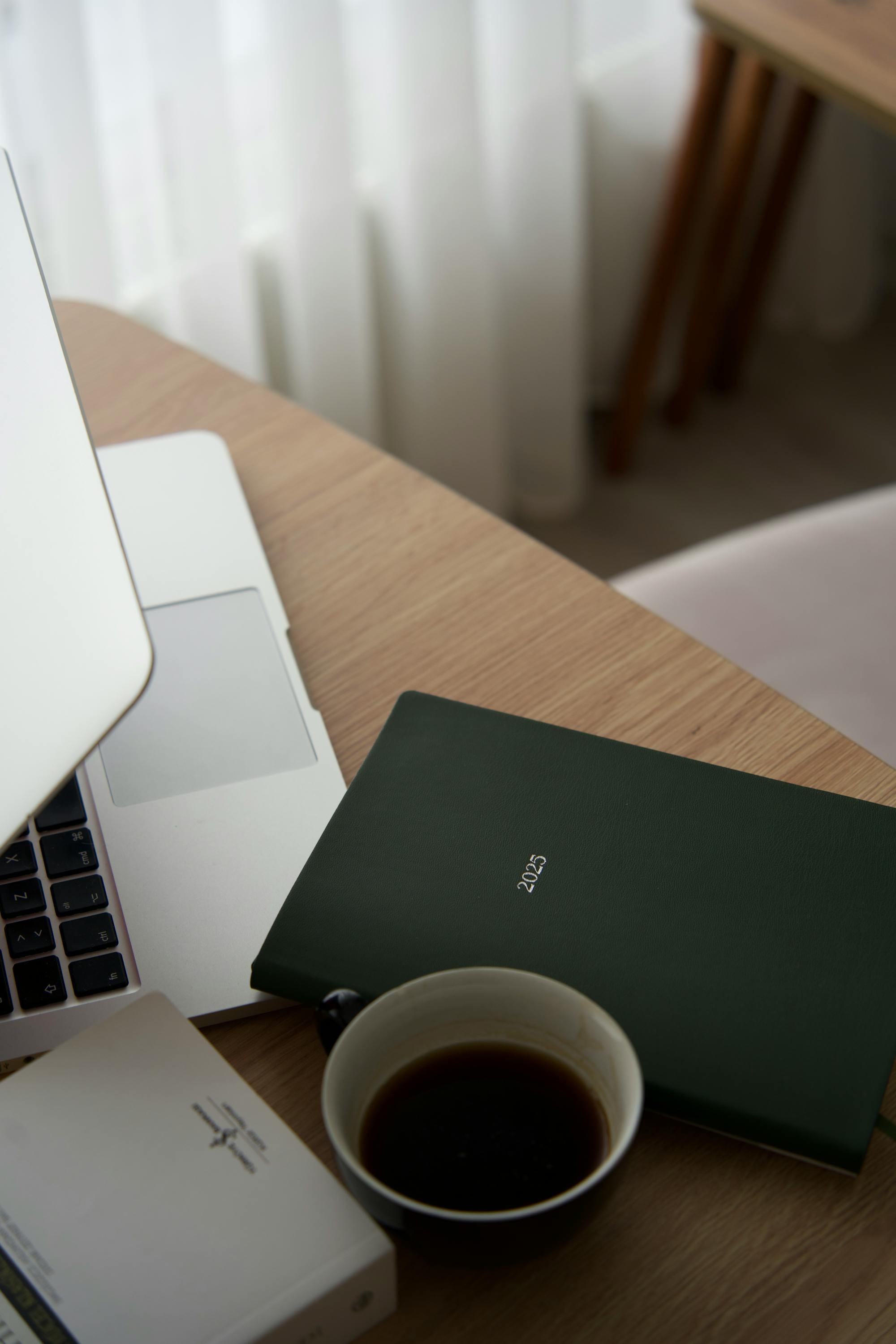 A calm, focused workspace — laptop, notebook, and morning coffee on a wooden desk.